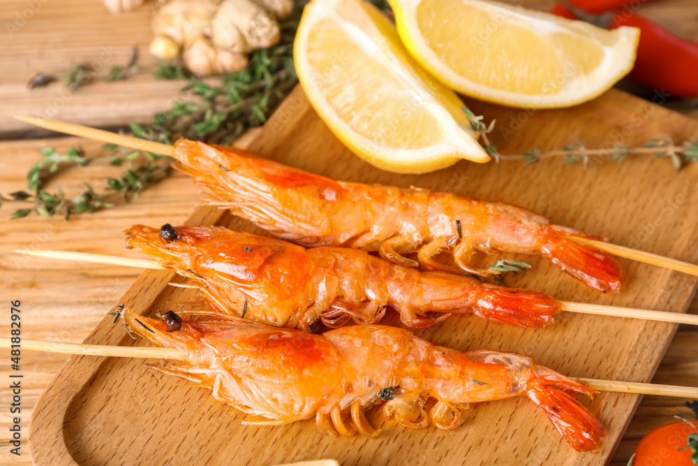 Board with grilled shrimp skewers on wooden background, closeup