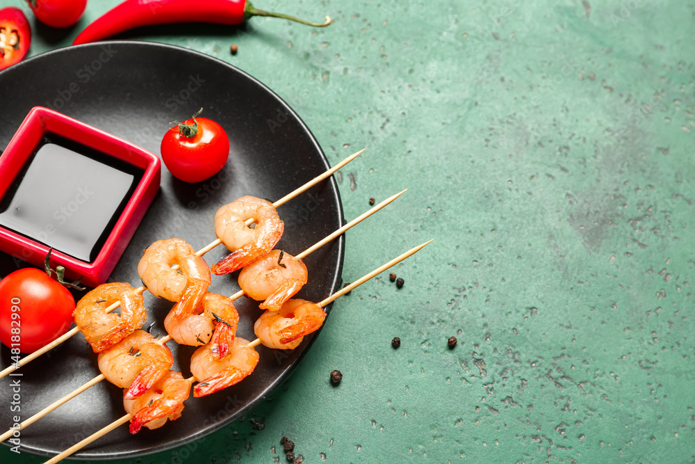 Plate with grilled shrimp skewers and sauce on green background