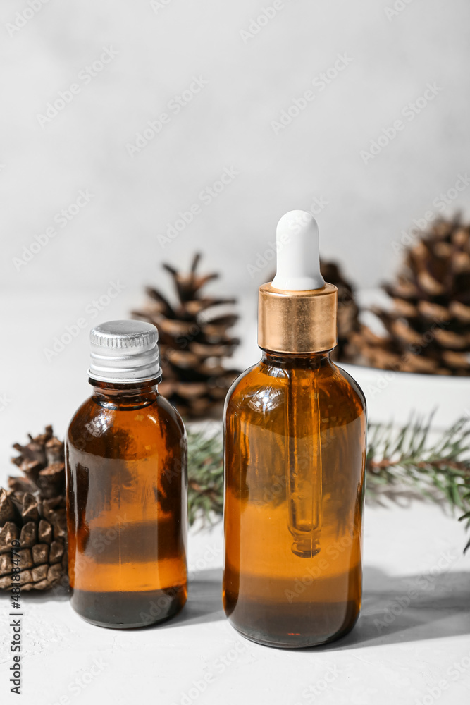 Bottles of essential oil and pine cones on light background, closeup