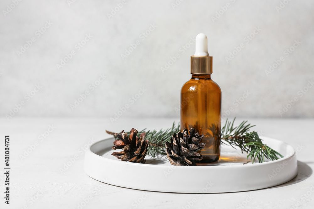 Plate with bottle of essential oil, fir branch and pine cones on light background