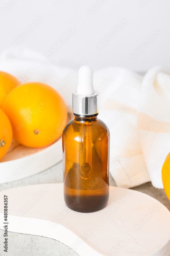 Bottle of essential oil and fresh oranges on light background, closeup