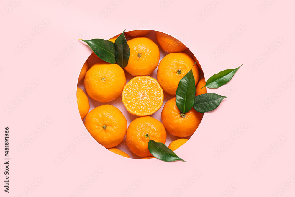 Composition with ripe tangerines and leaves on pink background