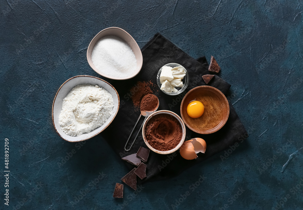 Bowl with cocoa powder and ingredients for preparing chocolate brownie on black background