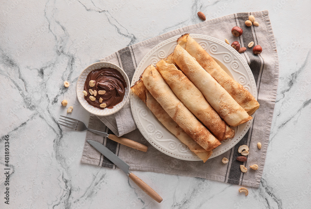 Plate of tasty thin pancakes with chocolate paste and nuts on white marble background