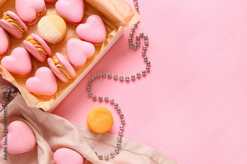 Box with tasty heart-shaped macaroons and beads on pink background