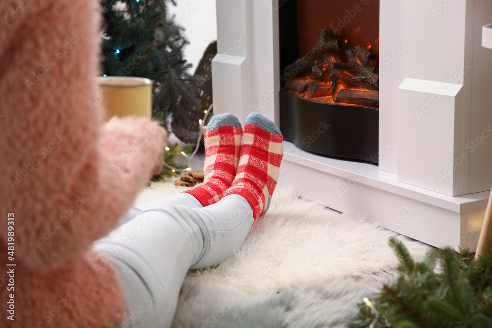 Woman in warm socks with cup near fireplace at home on Christmas eve, closeup