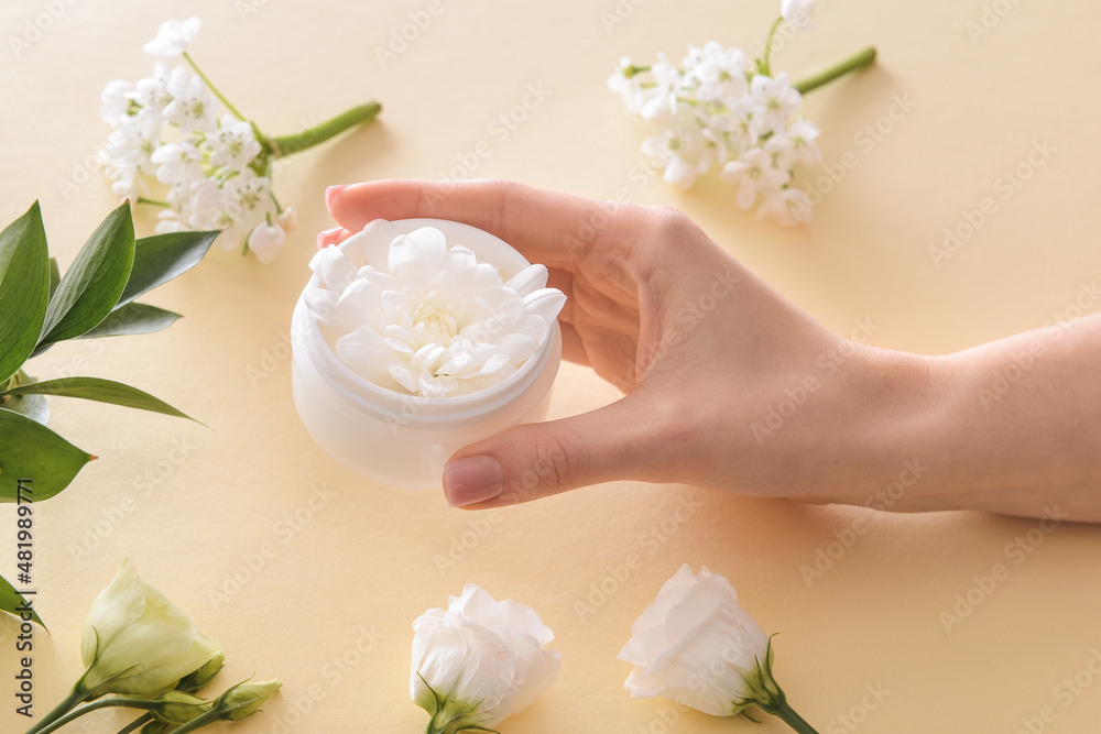 Female hand with cosmetic cream and flowers on light background