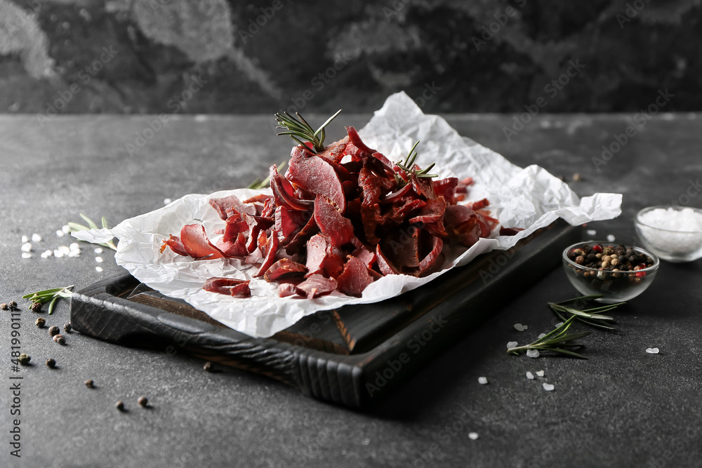 Board with spicy beef jerky on dark background