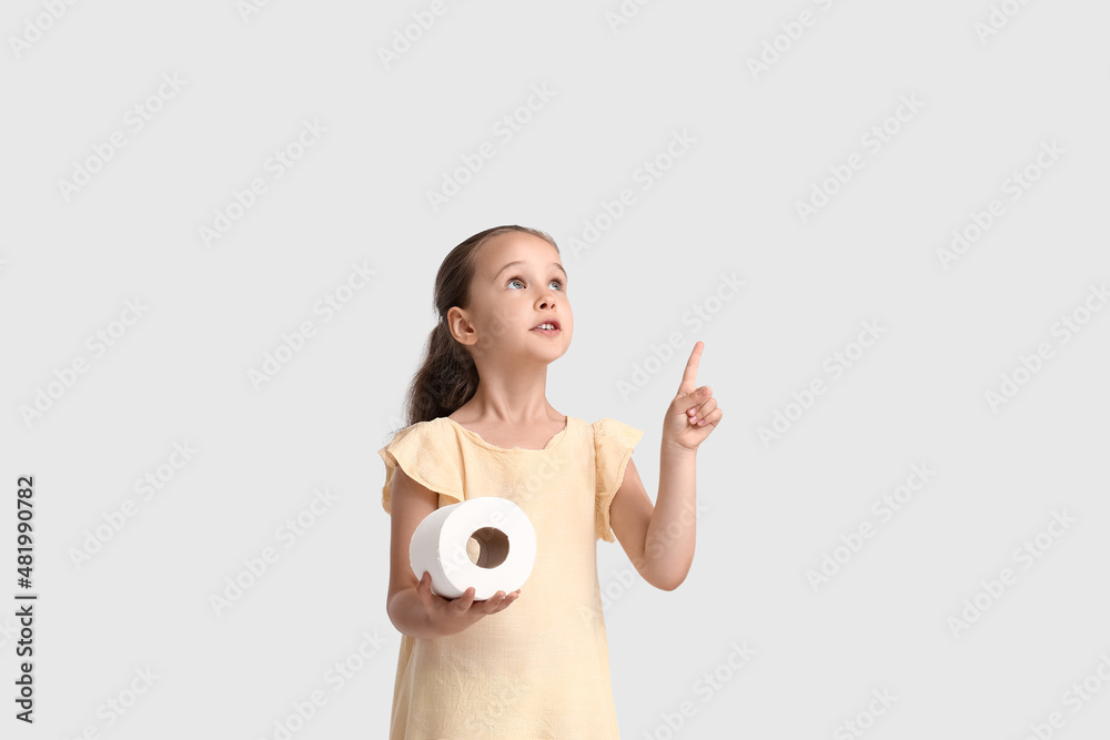 Cute little girl with toilet paper pointing at something on light background