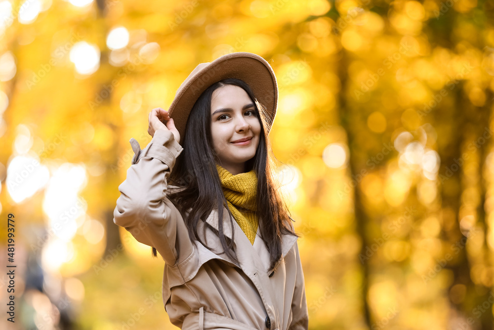 Young smiling woman wearing felt hat in autumn park on sunny day