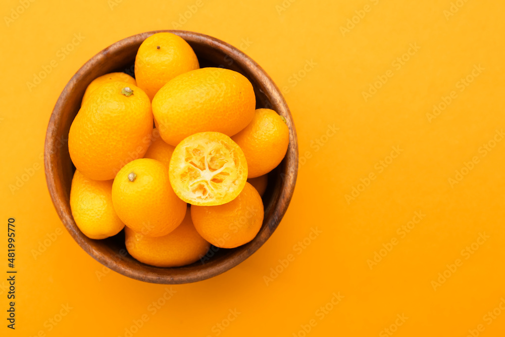 Bowl with tasty kumquat fruits on orange background