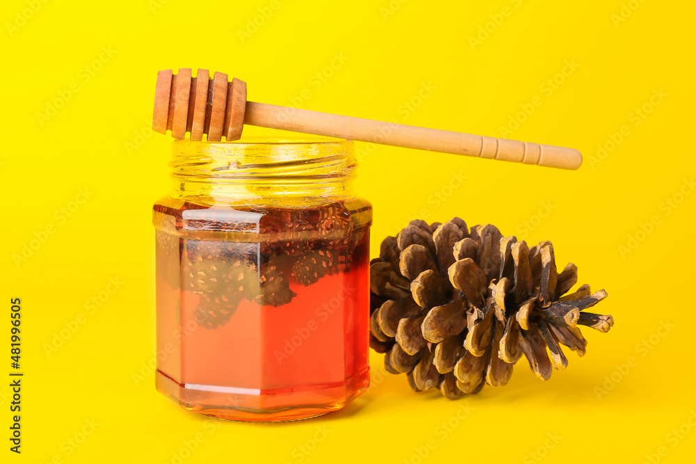 Jar of tasty pine cone jam and dipper on yellow background