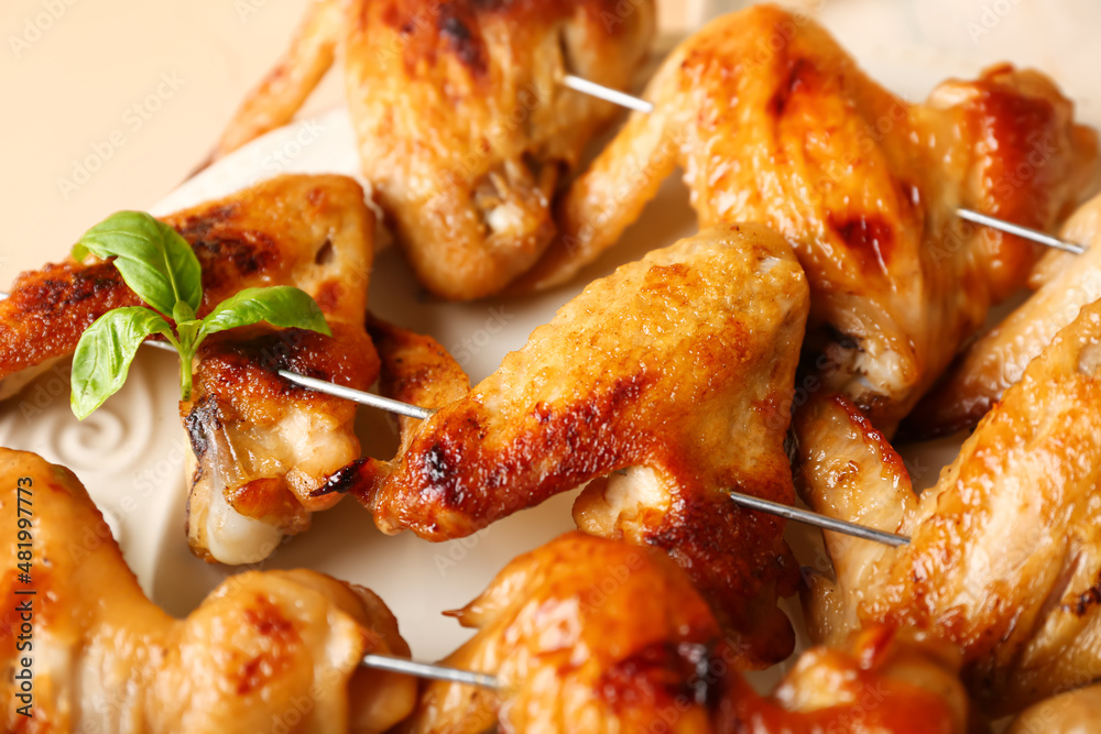 Plate with grilled chicken wings skewers on beige background, closeup