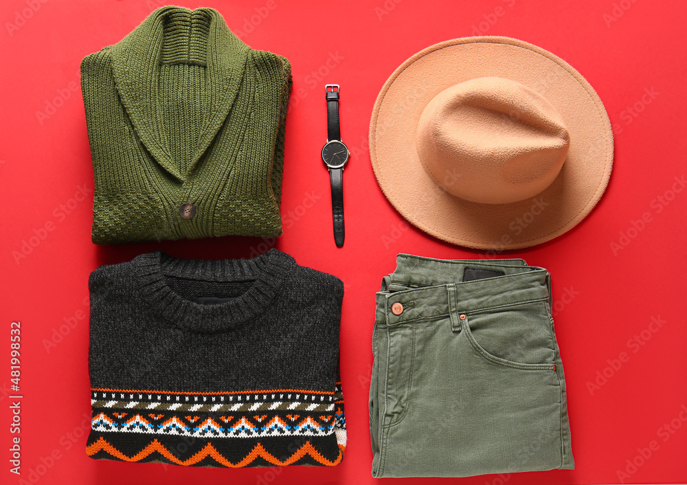 Male sweaters, pants, felt hat and wristwatch on red background