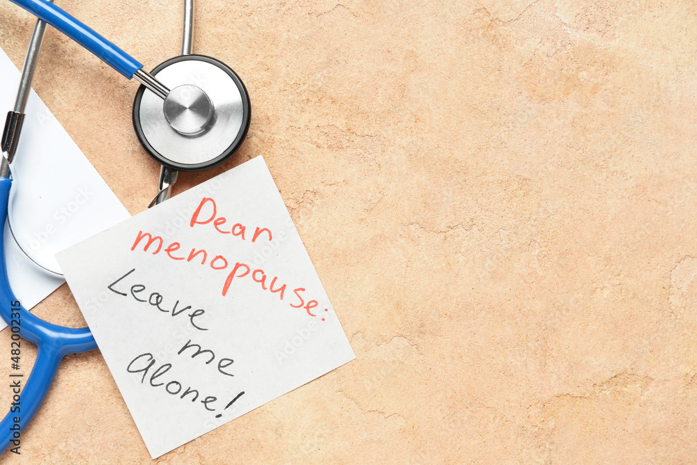 Sticky note with text DEAR MENOPAUSE LEAVE ME ALONE and stethoscope on beige background