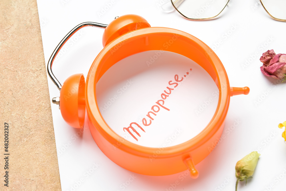 Paper sheet with word MENOPAUSE and alarm clock on beige background, closeup