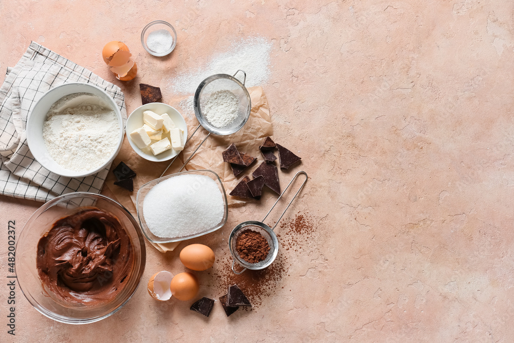 Bowl with fresh dough and ingredients for preparing chocolate brownie on beige background