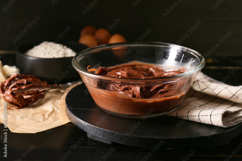 Bowl with fresh dough for preparing chocolate brownie on black background