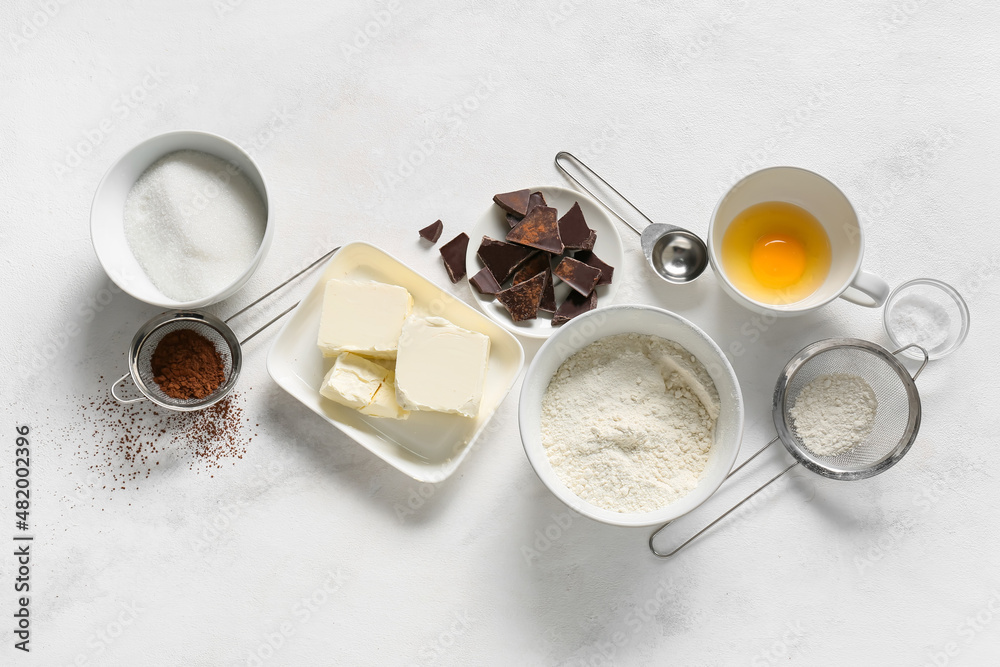 Bowl with butter and ingredients for preparing chocolate brownie on white background