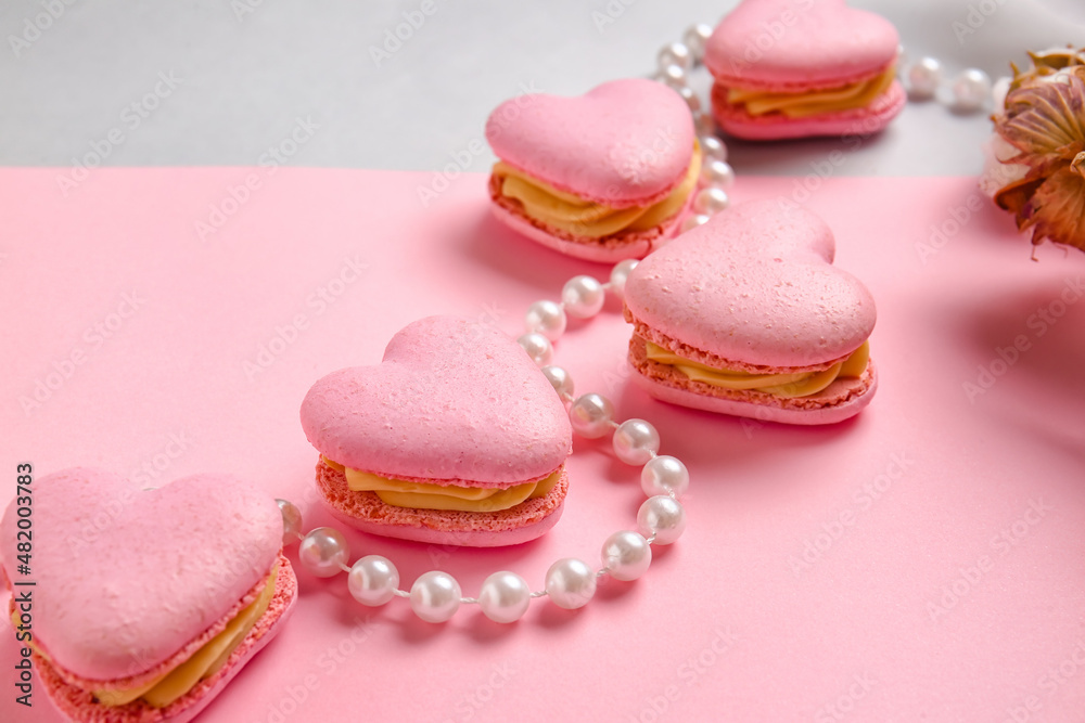 Tasty heart-shaped macaroons and beads on color background, closeup