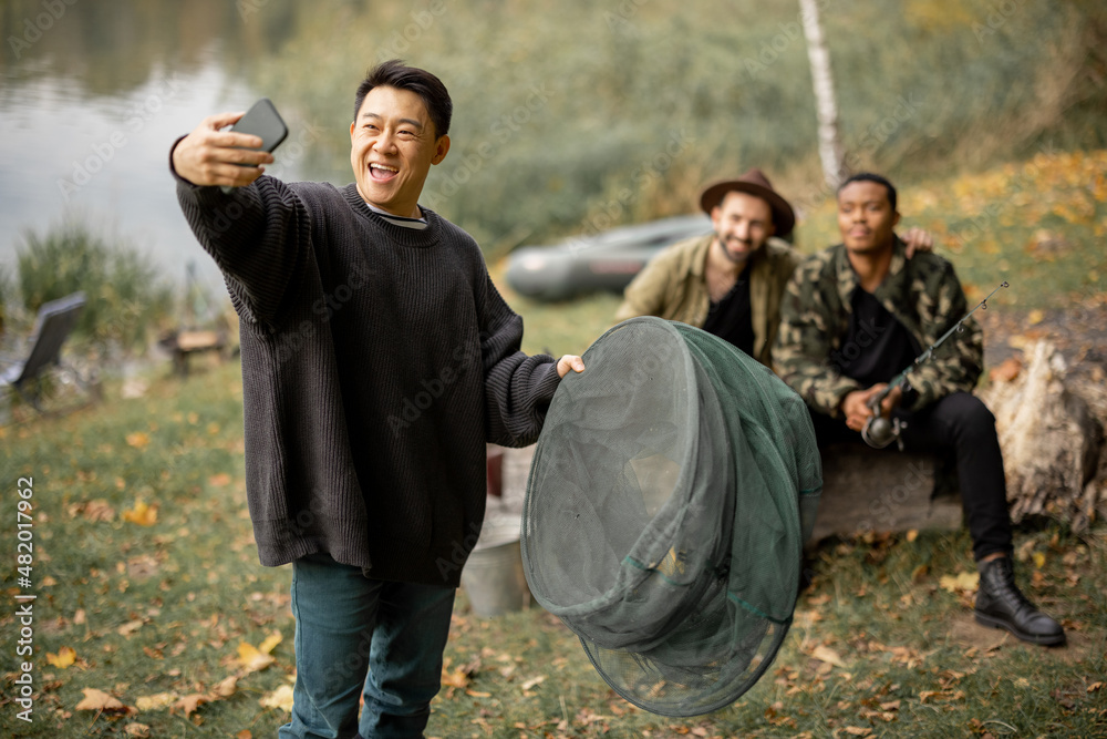 亚洲男子与多种族男性朋友在智能手机上自拍。男子休息和消磨时间t