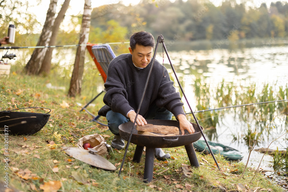 Korean man making fire in grill for cooking at nature. Concept of leisure, weekend, hobby and vacati