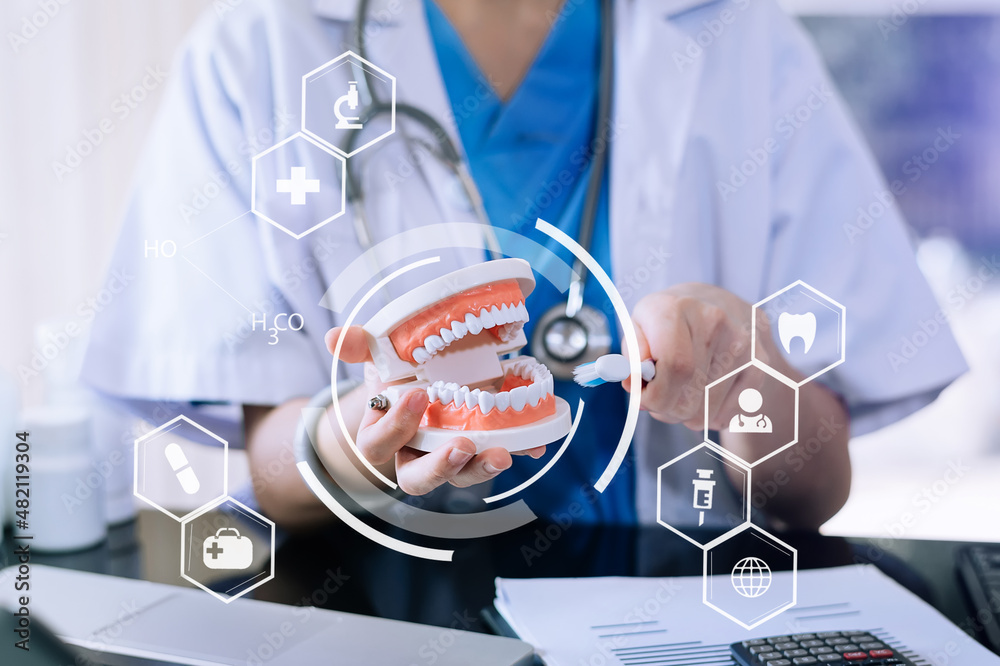 Concentrated dentist sitting at table with jaw samples tooth model and working with tablet and lapto