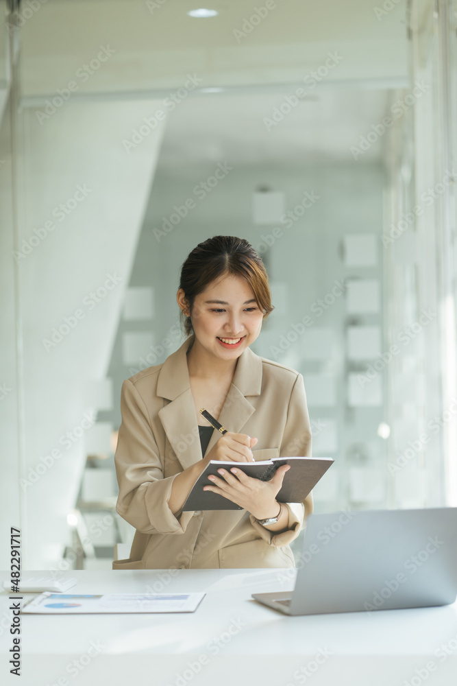 年轻的亚洲女性在家学习时记笔记并使用笔记本电脑，女性在客厅放松