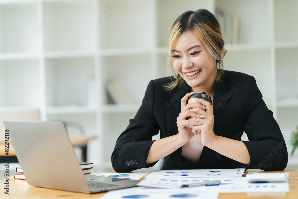 年轻的亚洲女商人有幸在平板电脑上观看工作和最喜欢的咖啡。