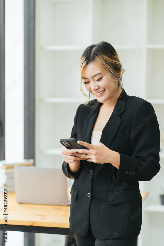 Successful young business woman using a smartphone while standing in front of her own business offic