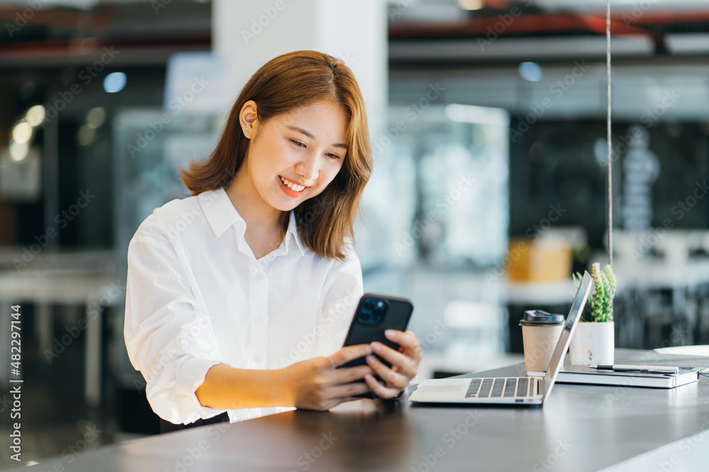 Asian young lady working in the cafe with laptop, holding phone smiling.