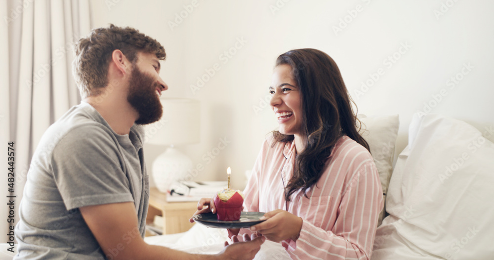 happy birthday to my beautiful wife. Shot of a young man surprising his wife with a cupcake in bed a