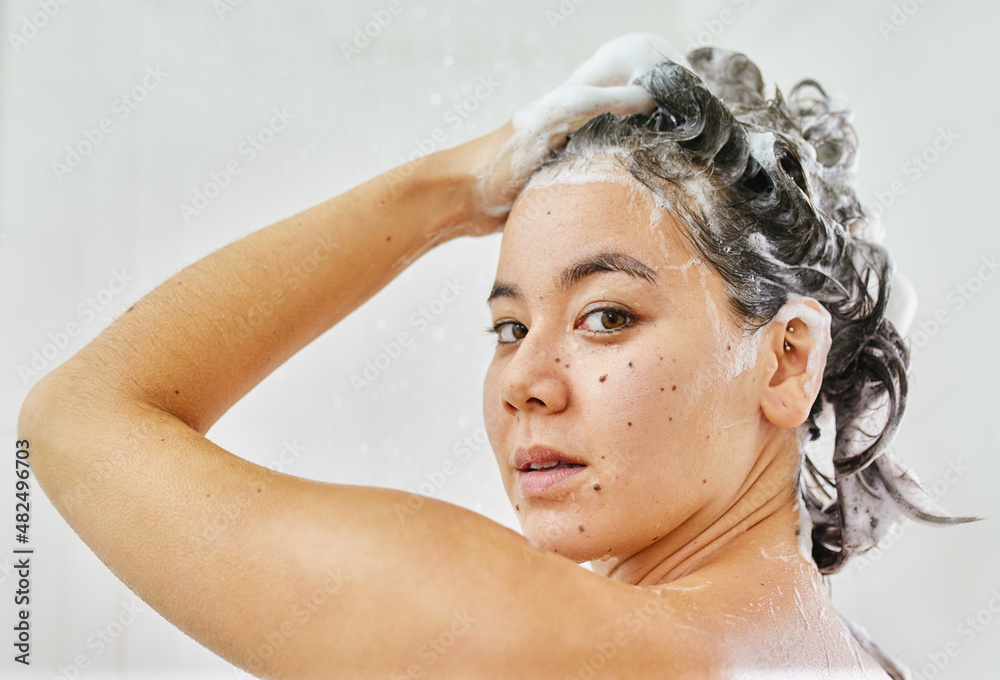 Getting her hair squeaky clean. Shot of a young woman washing her hair with shampoo in the shower at