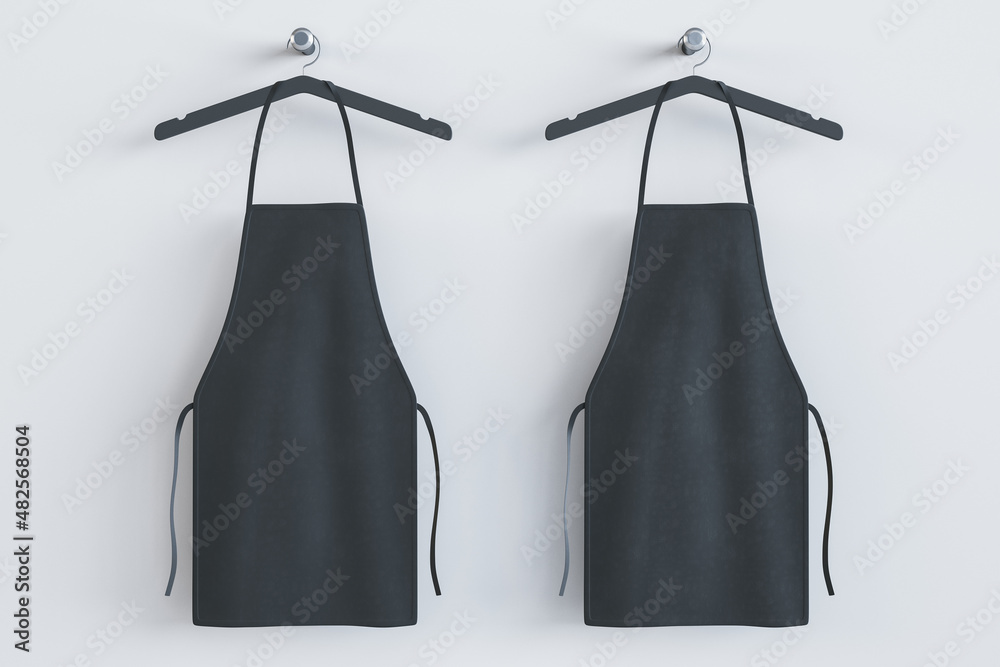 Empty black kitchen aprons on hangers. Light background. Chef and cooking concept. Mock up place. 3D