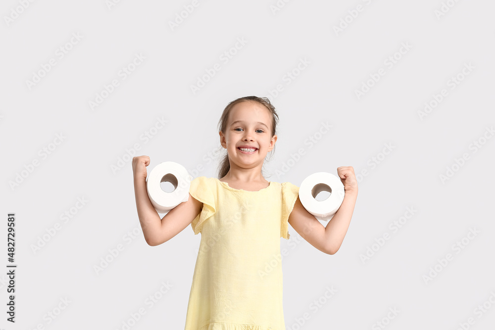 Funny little girl with rolls of toilet paper on light background