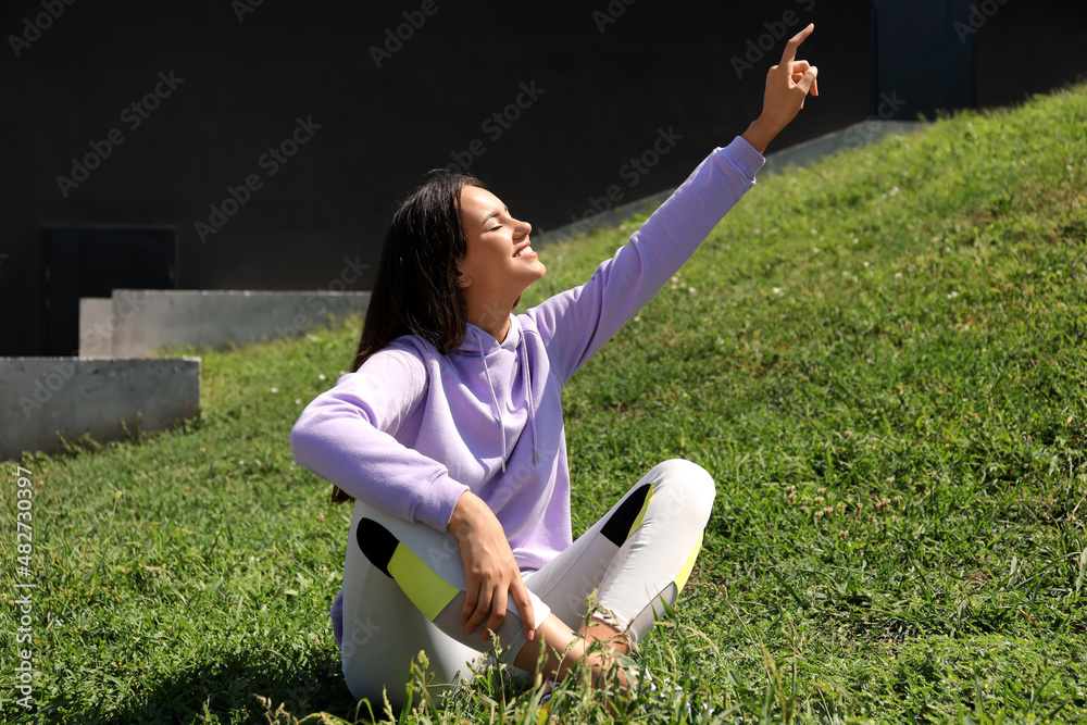 Beautiful young woman in stylish hoodie pointing at something outdoors