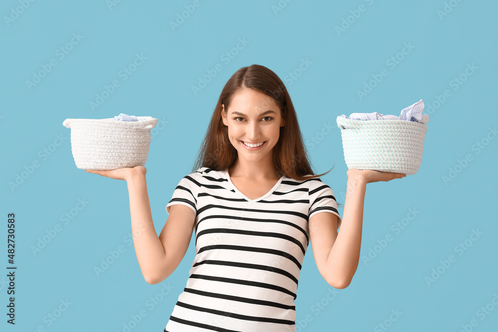 Beautiful housewife with laundry in small baskets on blue background