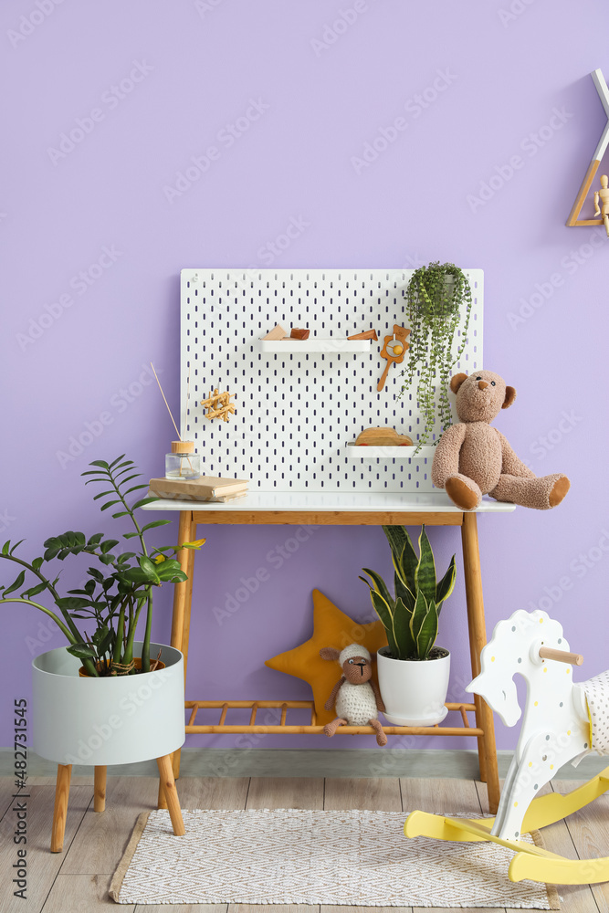 Table with pegboard, toys and houseplants near lilac wall