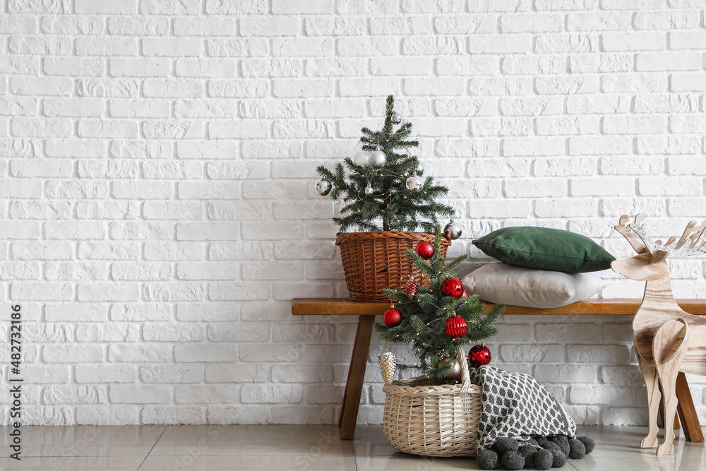 Beautiful Christmas trees near white brick wall in interior of room