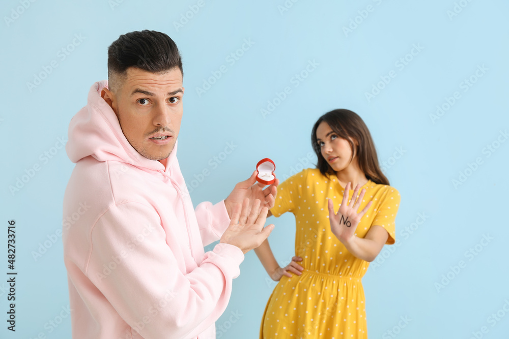 Young woman rejecting marriage proposal on blue background