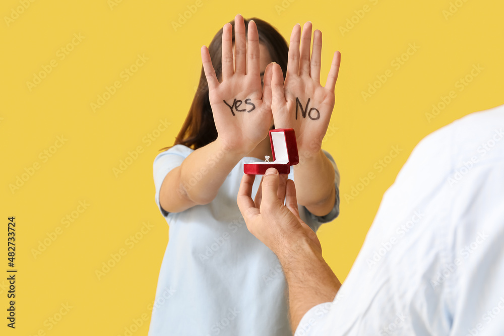 Young man proposing to his hesitating girlfriend on color background