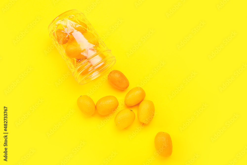 Jar with tasty kumquat fruits on yellow background