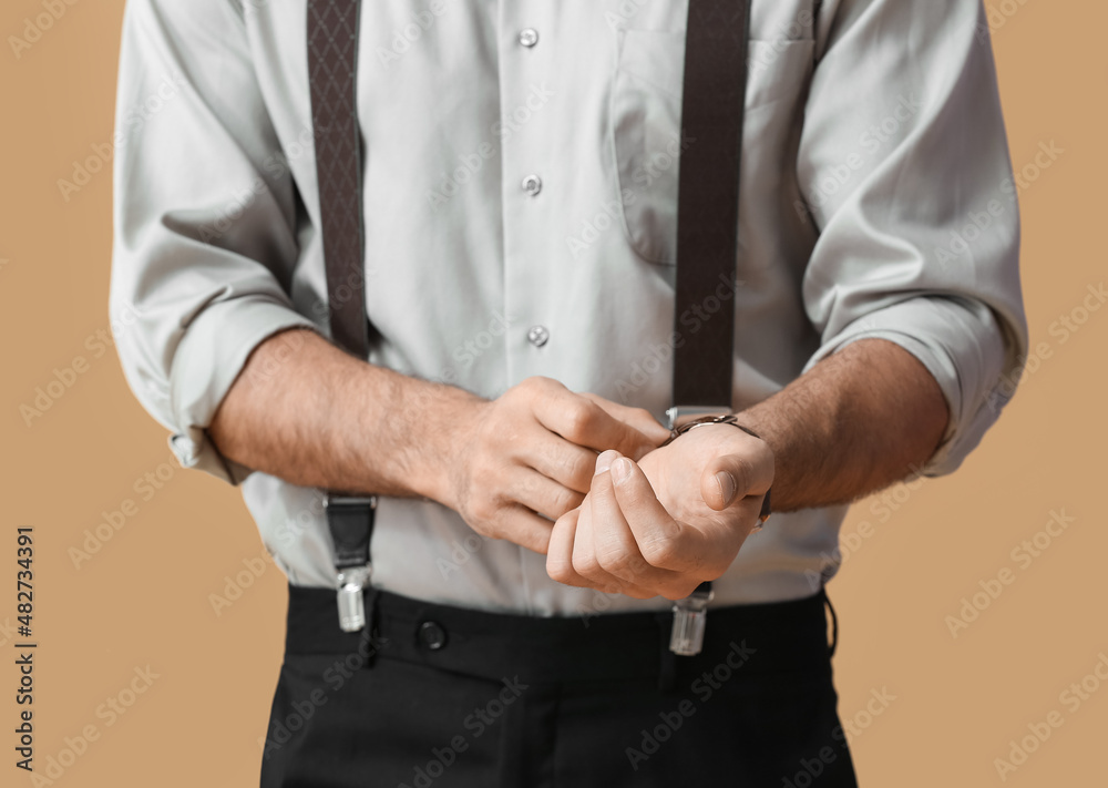 Fashionable gentleman adjusting wristwatch on color background, closeup