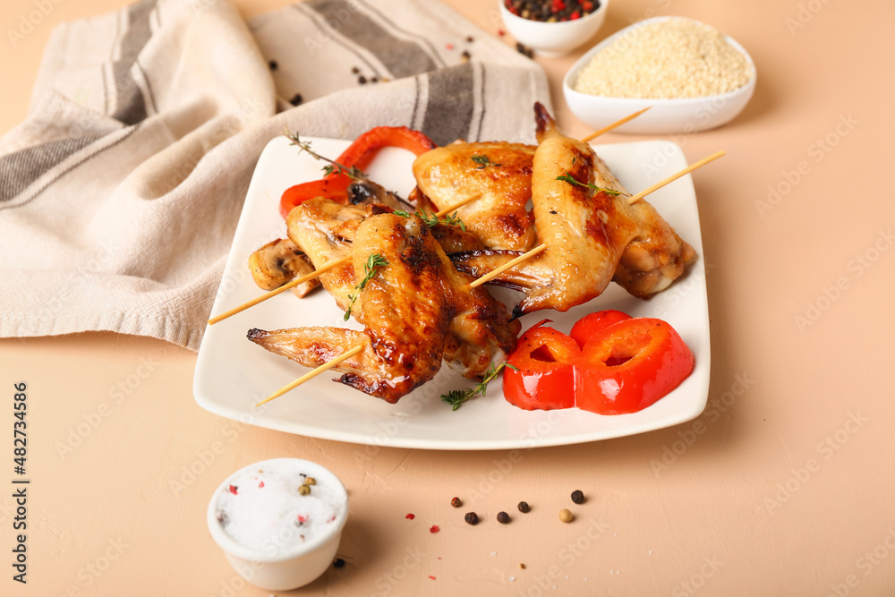 Plate with grilled chicken wings skewers on beige background