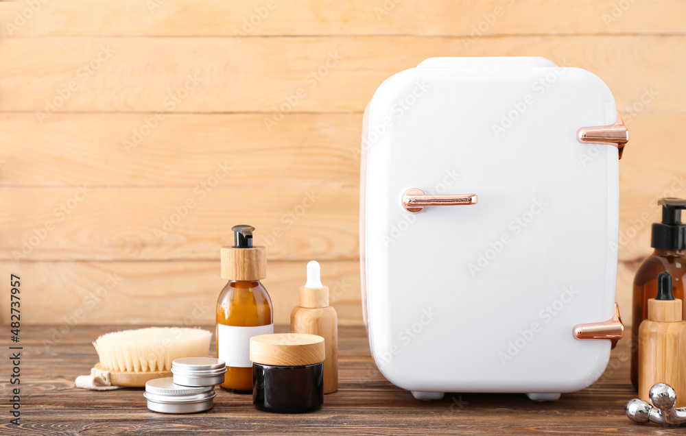 Small refrigerator and cosmetic products on wooden table