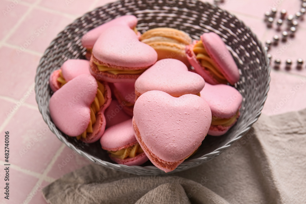 Bowl with tasty heart-shaped macaroons on pink background, closeup