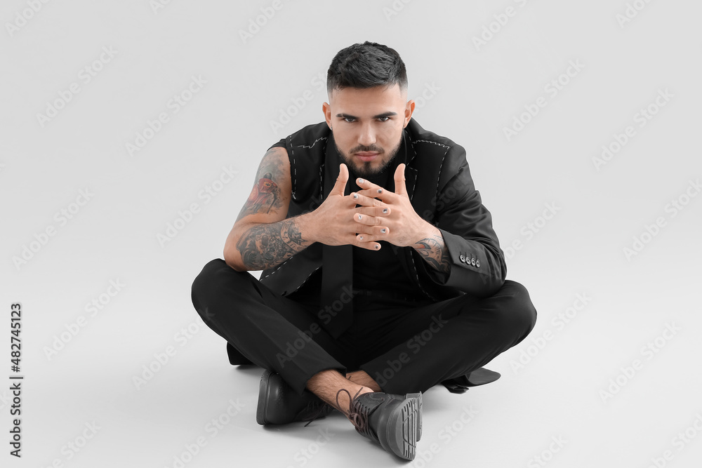 Young man with stylish manicure and crossed fingers in unfinished suit on light background