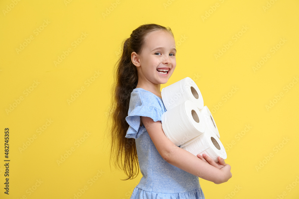 Funny little girl with rolls of toilet paper on yellow background