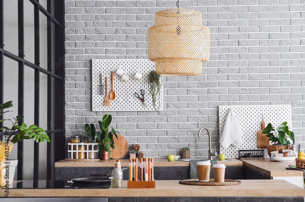 Interior of stylish kitchen with modern furniture and pegboard on grey brick wall