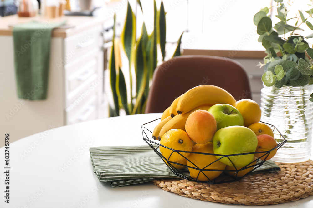 Basket with fresh fruits on table in light room